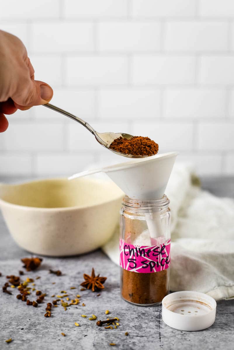 spooning chinese five spice into glass container