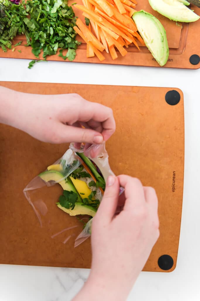 child folding top of spring roll wrapper down over filling