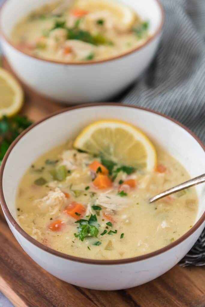 two bowls of lemon chicken soup with lemon slices and spoons in bowls