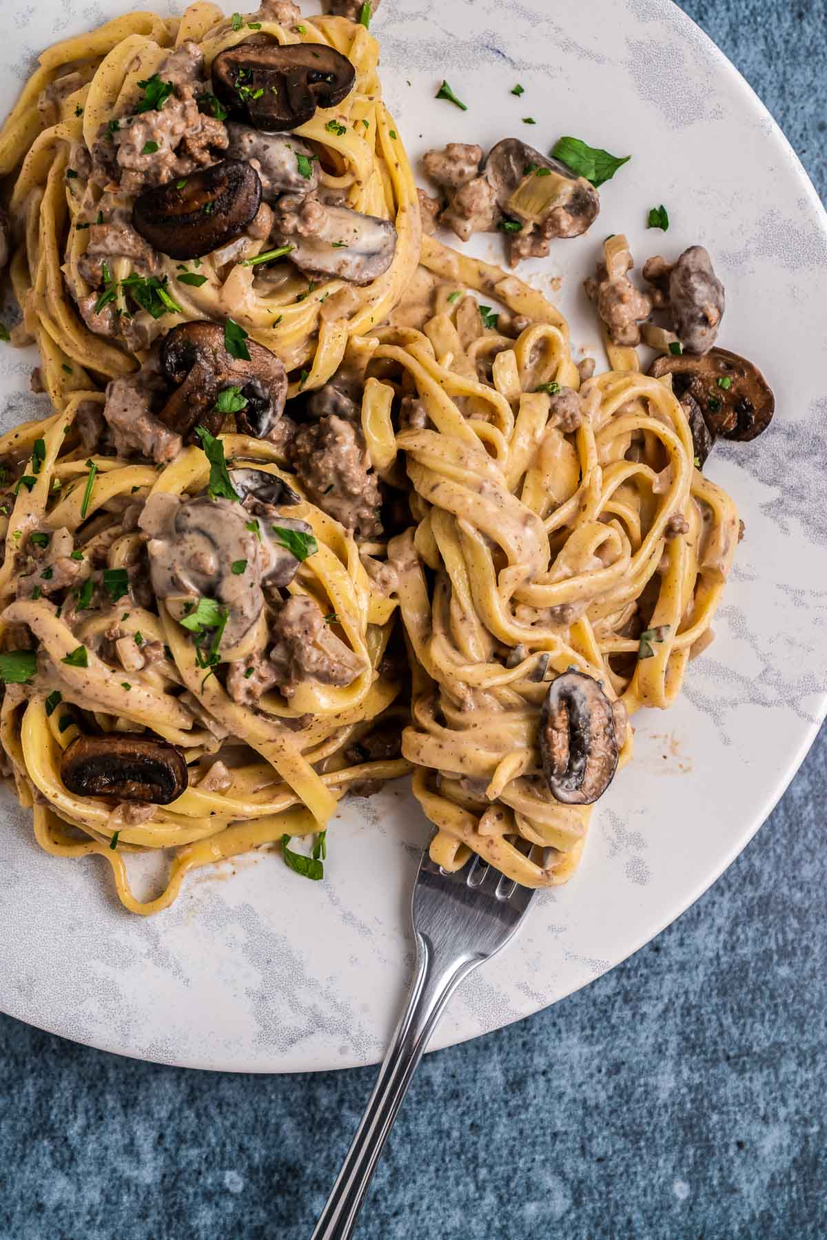 white plate with ground beef stroganoff with fork twirled in noodles