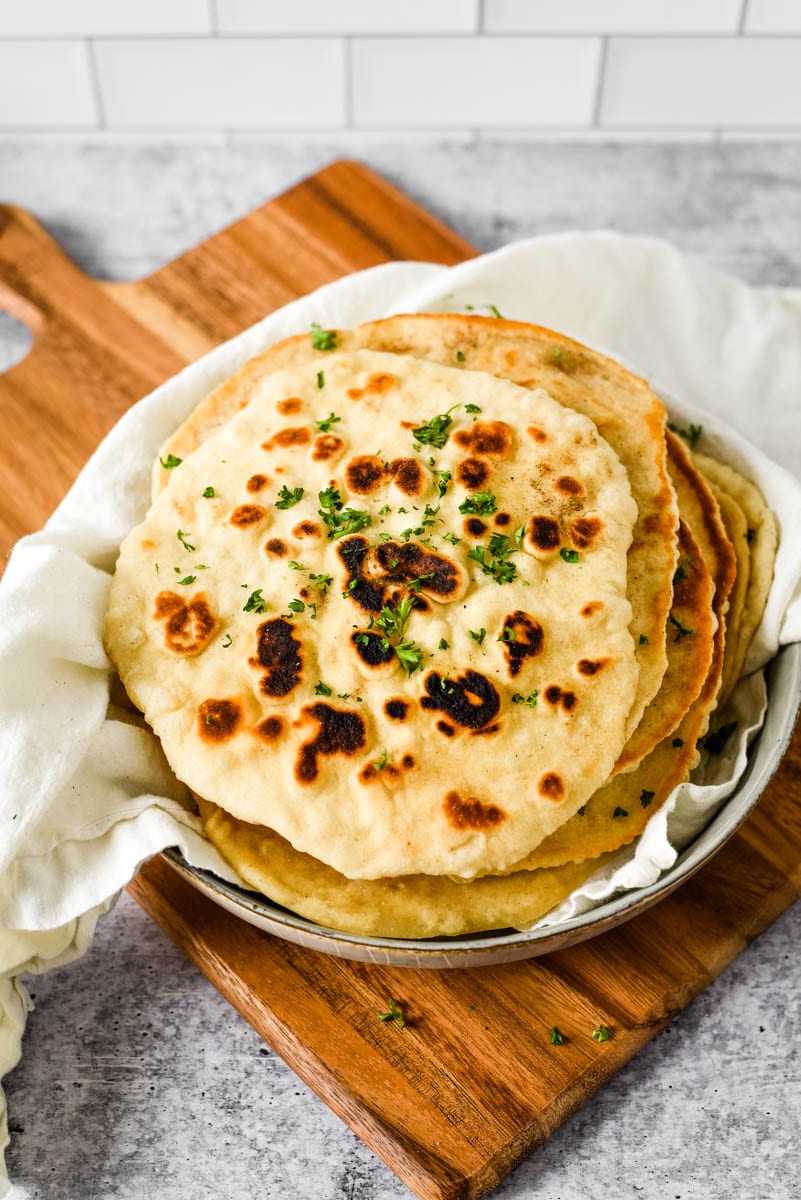 sourdough naan in bowl on wooden cutting board