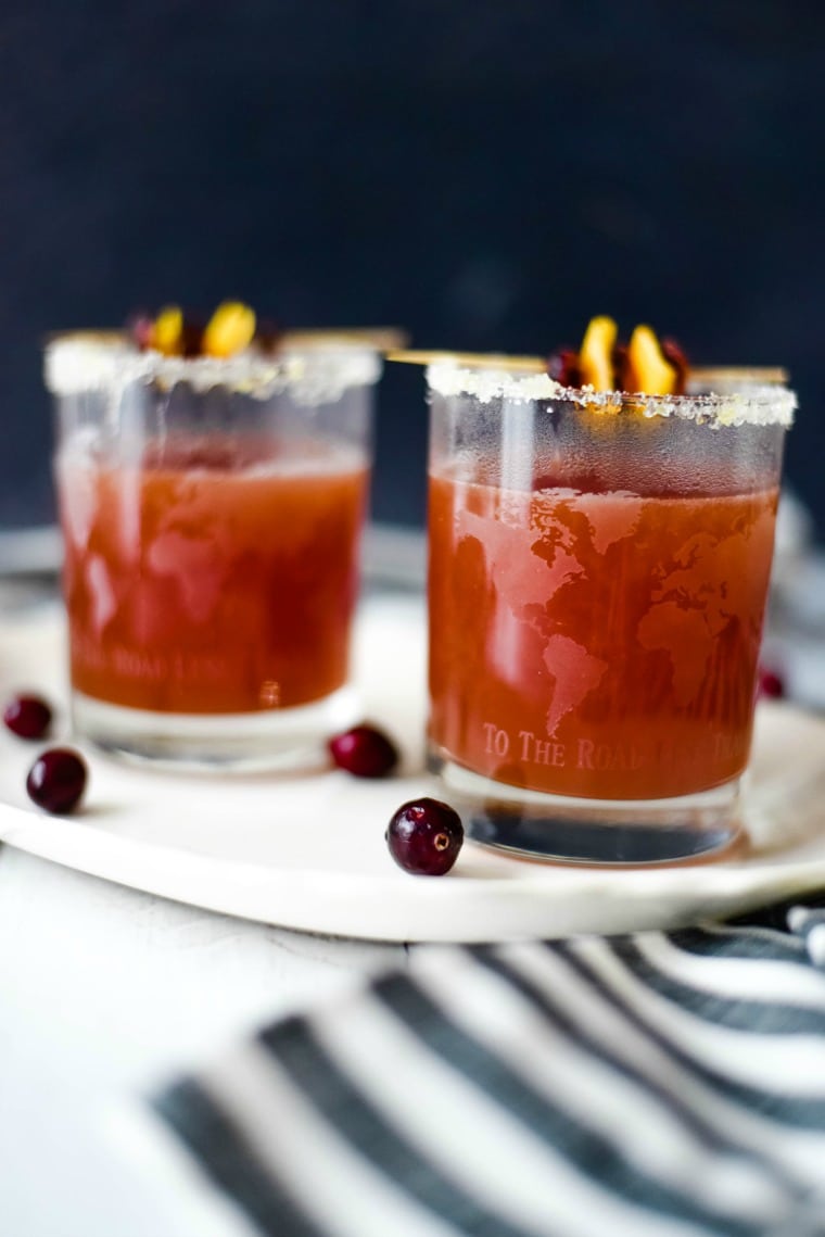 two glasses of cranberry orange cocktails on a plate with cranberries